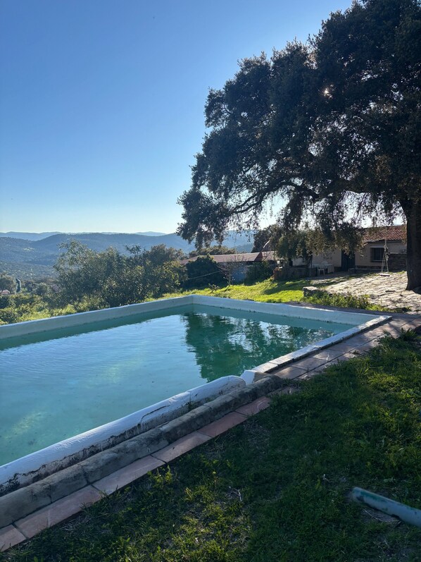 A swimming pool with a view of distant hills, surrounded by greenery and a building.