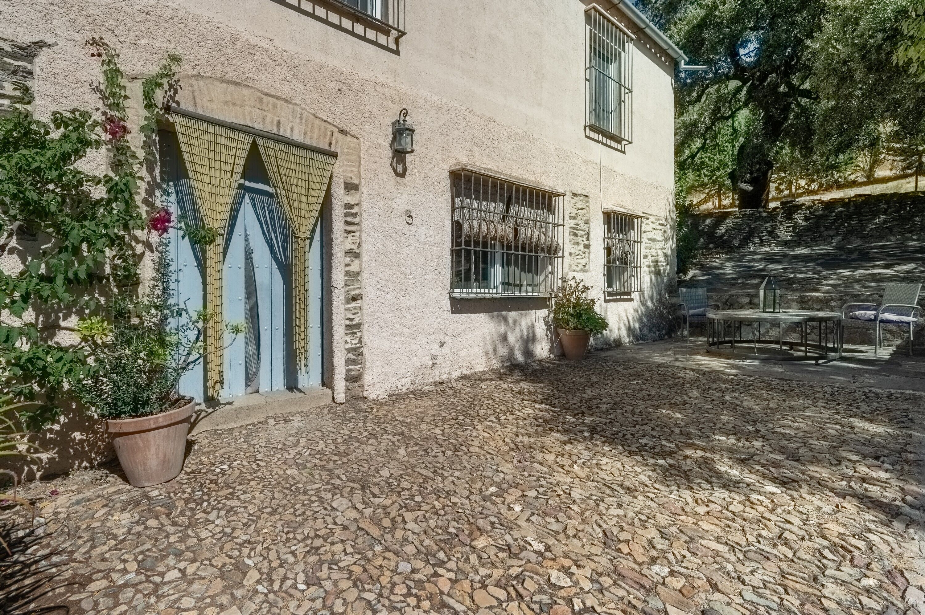 Un patio empedrado con un edificio rústico, plantas en macetas y mobiliario exterior.