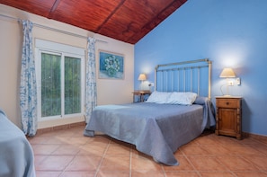 A bedroom with a bed, a nightstand, a lamp, a window with curtains, and a painting on the wall.