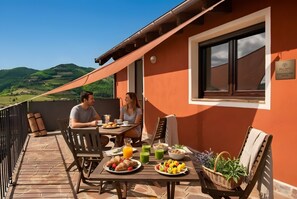 Una terrazza con un tavolo apparecchiato per la colazione, vista su dolci colline e un cartello che indica servizi benessere.
