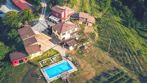 An aerial view of a residential area with terraced vineyards, a swimming pool, and several houses with red roofs.