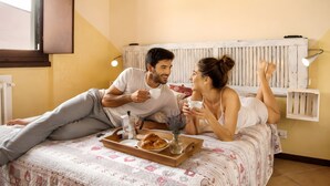 A couple on a bed with a tray of food and drinks, a window, and a radiator.