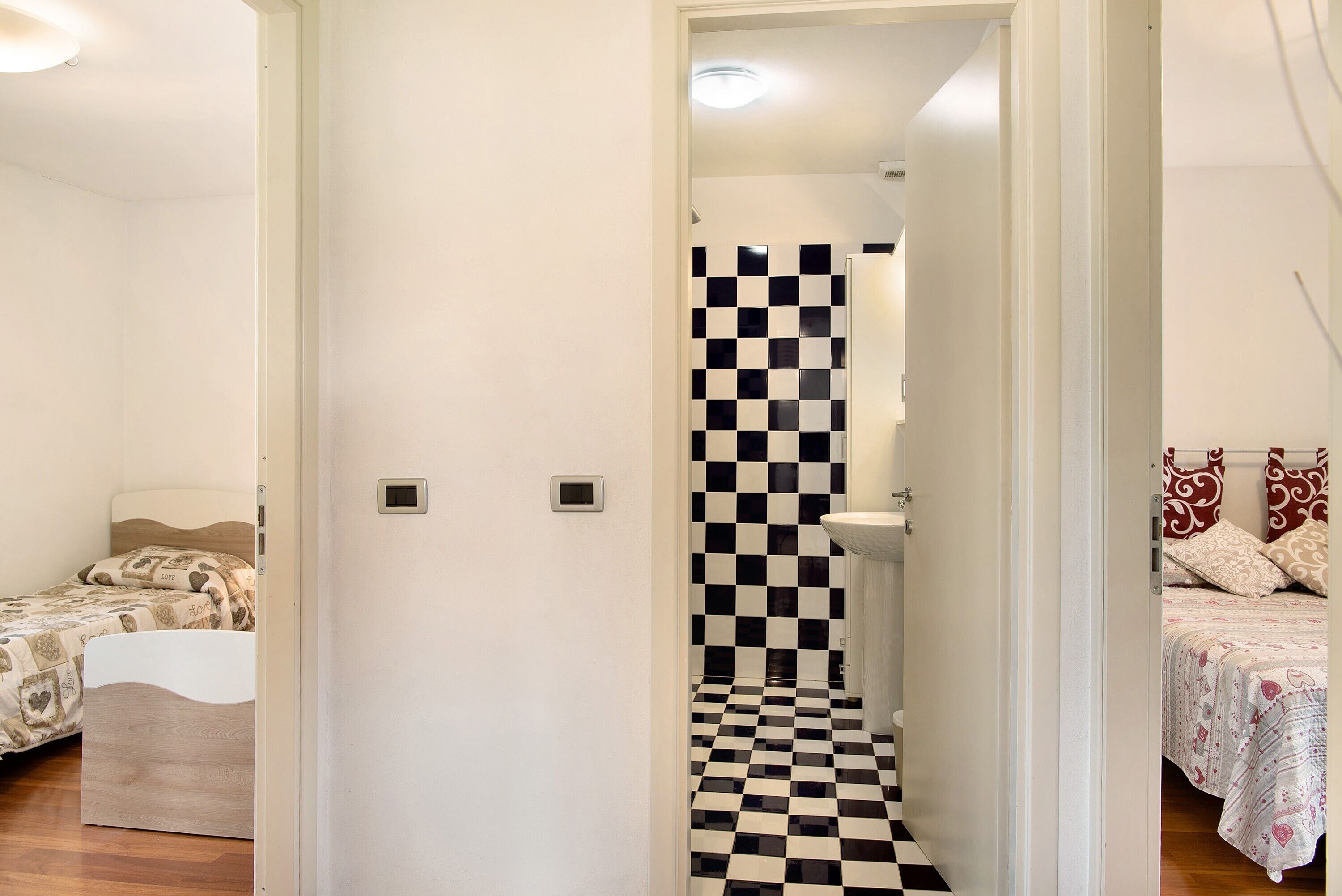 A bedroom with a checkered floor, a bed with patterned bedding, and a white door leading to a bathroom with a checkered wall.