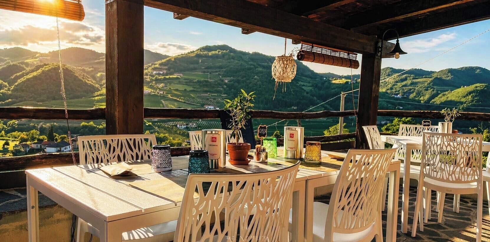 Un área de comedor al aire libre con mesas y sillas, un lámpara colgante y vistas a colinas verdes.