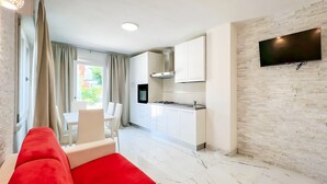 Una cocina moderna con armarios blancos, un televisor de pantalla plana montado en una pared de ladrillo y una zona de comedor con un sofá rojo.