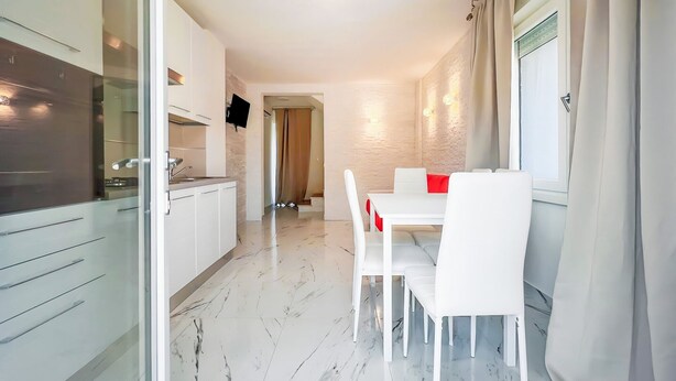 Una cocina moderna con armarios blancos, un comedor con sillas y mesa blancos, y un piso de mármol.