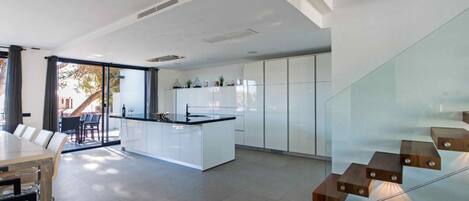 Une cuisine moderne avec des meubles blancs, un îlot central et un coin repas comprenant une table et des chaises.