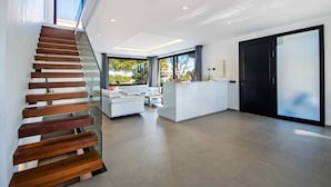 Un intérieur moderne avec un escalier en bois, un canapé blanc et une grande fenêtre donnant sur un paysage verdoyant.