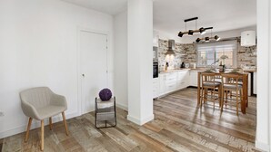 Een moderne keuken met houten vloeren, witte keukenkastjes en een eethoek met een houten tafel en stoelen.