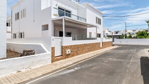 Un edificio moderno blanco de dos pisos con balcón, un camino de entrada pavimentado y cielo despejado.
