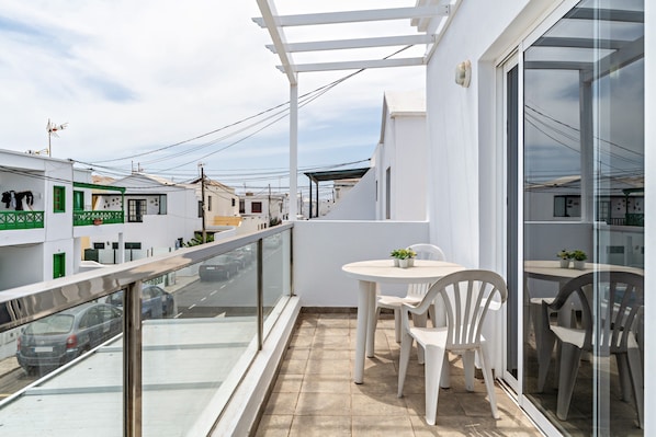 A balcony with a glass railing, a white table with chairs, and a view of the street below.