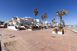 A coastal building with balconies, palm trees, and a clear sky.