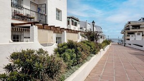 Un edificio blanco con balcones, un camino pavimentado y vista al mar.