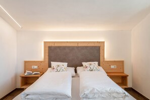 A hotel room with two beds, wooden headboards, bedside tables, and a built-in light fixture.