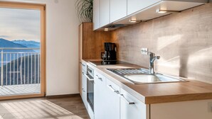 A modern kitchen with a large window, wooden cabinets, a sink, and a coffee maker. - Apartment "Reiterhof Gaia" with Mountain View, Private Garden & Wi-Fi (San Genesio Atesino)