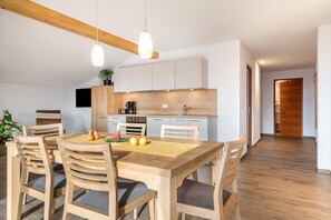 A modern kitchen with wooden cabinets, a dining table with chairs, and pendant lighting.