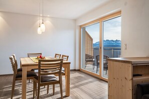 Comedor con mesa y sillas de madera, lámpara colgante y vistas a las montañas a través de un gran ventanal corredero.
