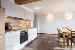 A modern kitchen with white cabinets, a wooden countertop, and a dining area with a wooden table and chairs.