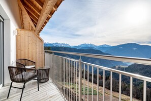 Un balcon doté d’un plafond en bois, d’une rambarde en métal et offrant une vue sur des montagnes enneigées.