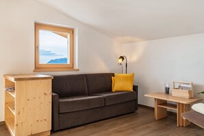Un salón moderno con una estantería de madera, un sofá marrón, una pequeña mesa de madera y una ventana con vistas a montañas.