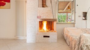 Une pièce avec une cheminée, un radiateur, un lit recouvert d’une couvre-lit à motifs floraux et une fenêtre donnant sur un paysage verdoyant.