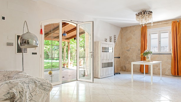 Une pièce comprenant un lit, une table blanche, un lustre, une porte donnant sur un espace extérieur et un mur en pierre.