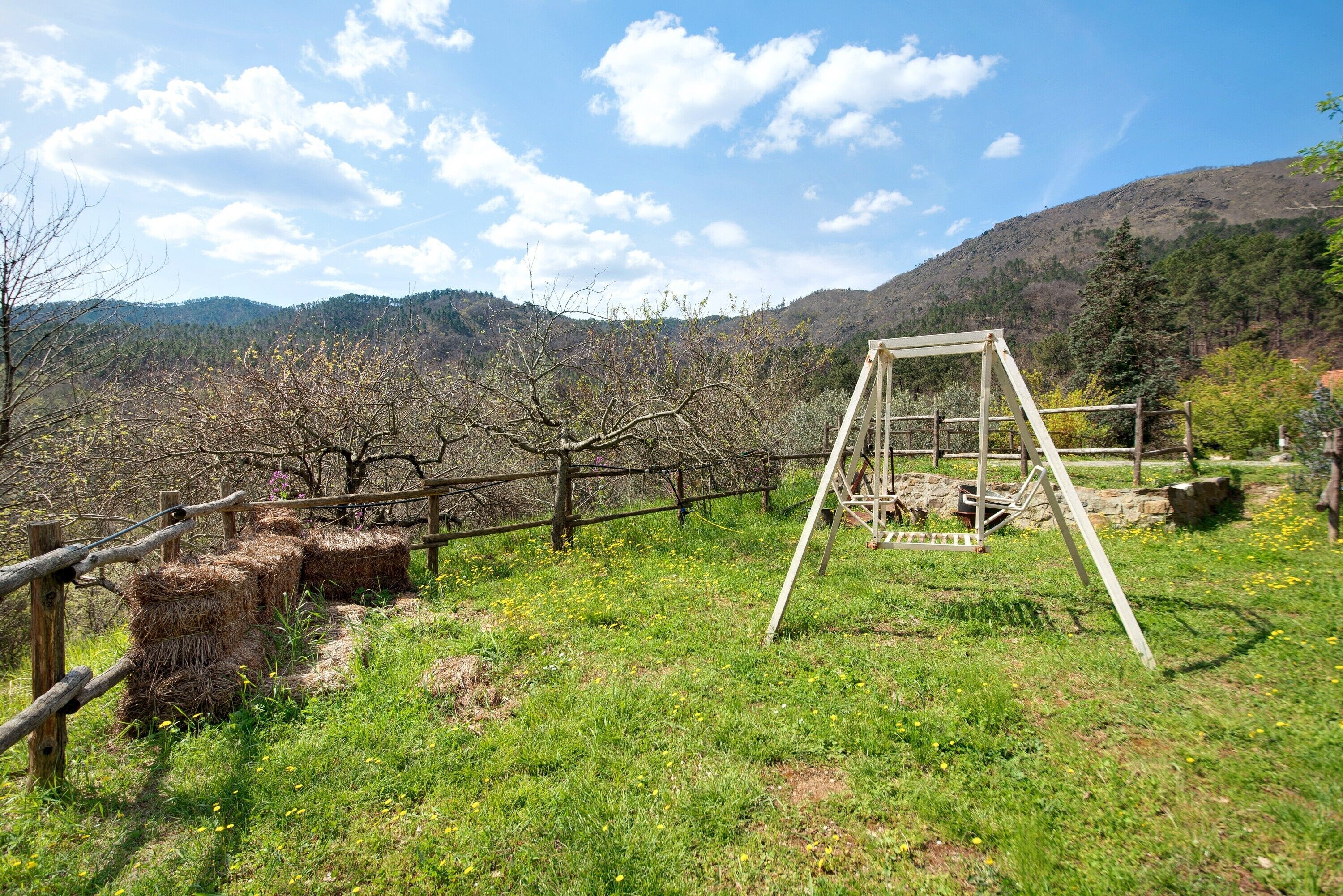 Un paysage rural avec une balançoire en bois, des bottes de foin et un mur de pierres.