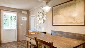 A dining area with a wooden table, chairs, a hanging light fixture, a wall-mounted map, and a door with a window.