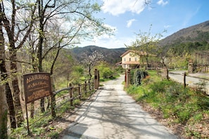 A rural road leading to a house with a sign indicating 'Agriturismo' and 'Allevamento' services.