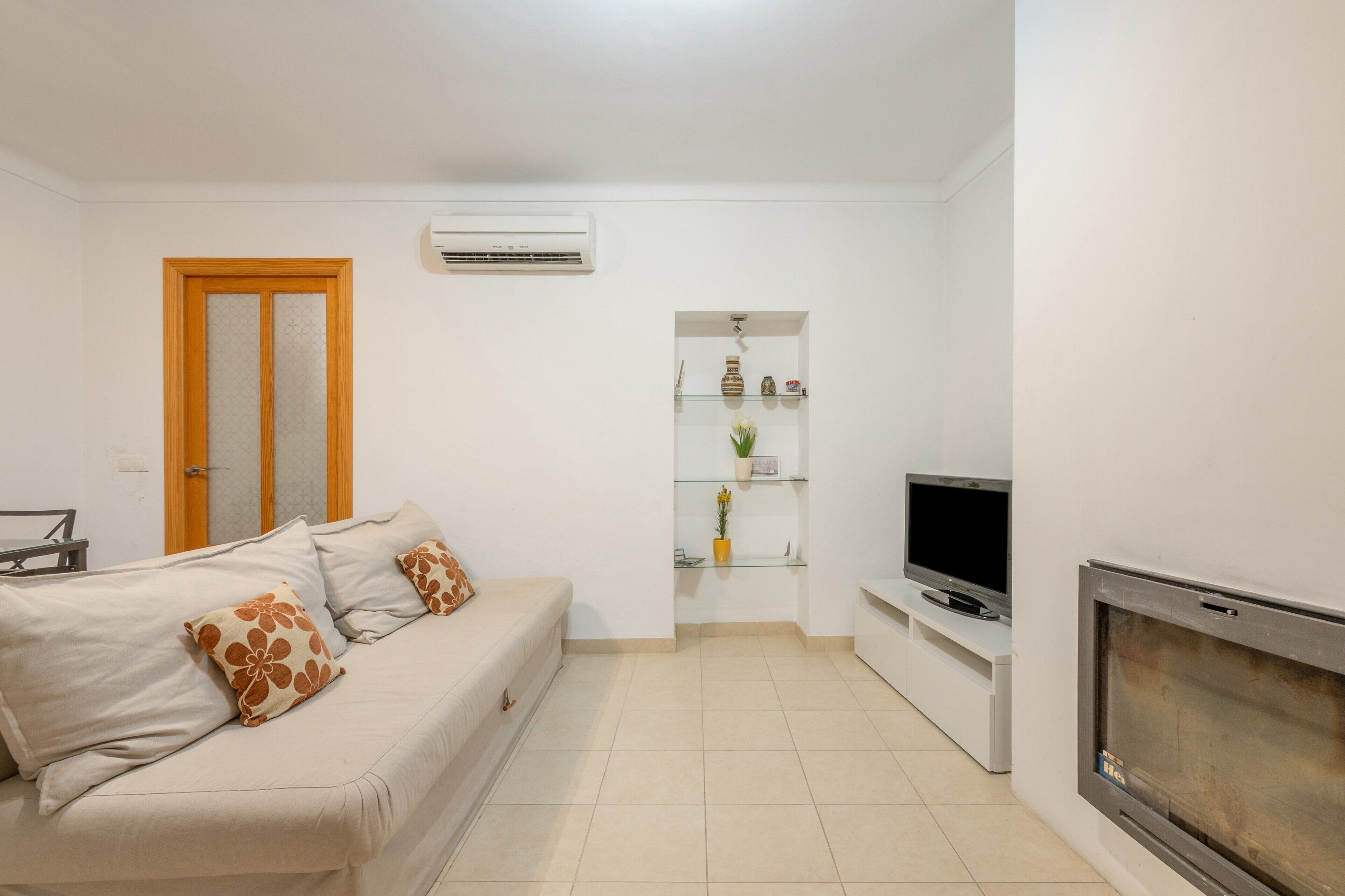 Uma sala de estar com sofá, televisão, lareira e uma estante com objetos decorativos.