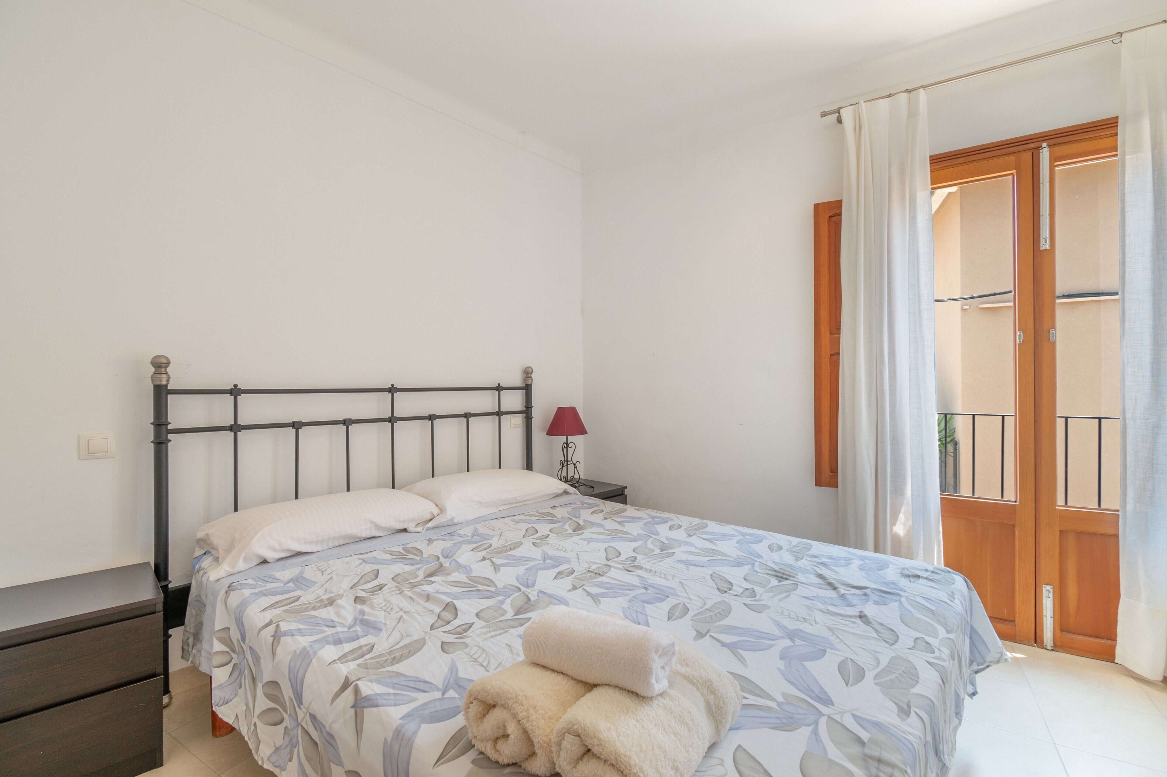 A bedroom with a bed, a nightstand, a lamp, and a view of an outdoor balcony.