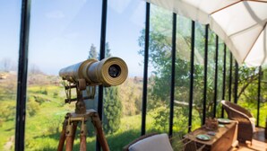A telescope on a tripod, a table with chairs, and a view of greenery through large windows. - Holiday Home 'Etnalodge' with Sea View, Private Terrace and Wi-Fi (Piedimonte Etneo)