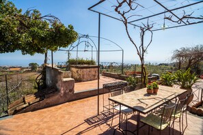 A patio with a table and chairs, surrounded by potted plants and a view of the landscape.