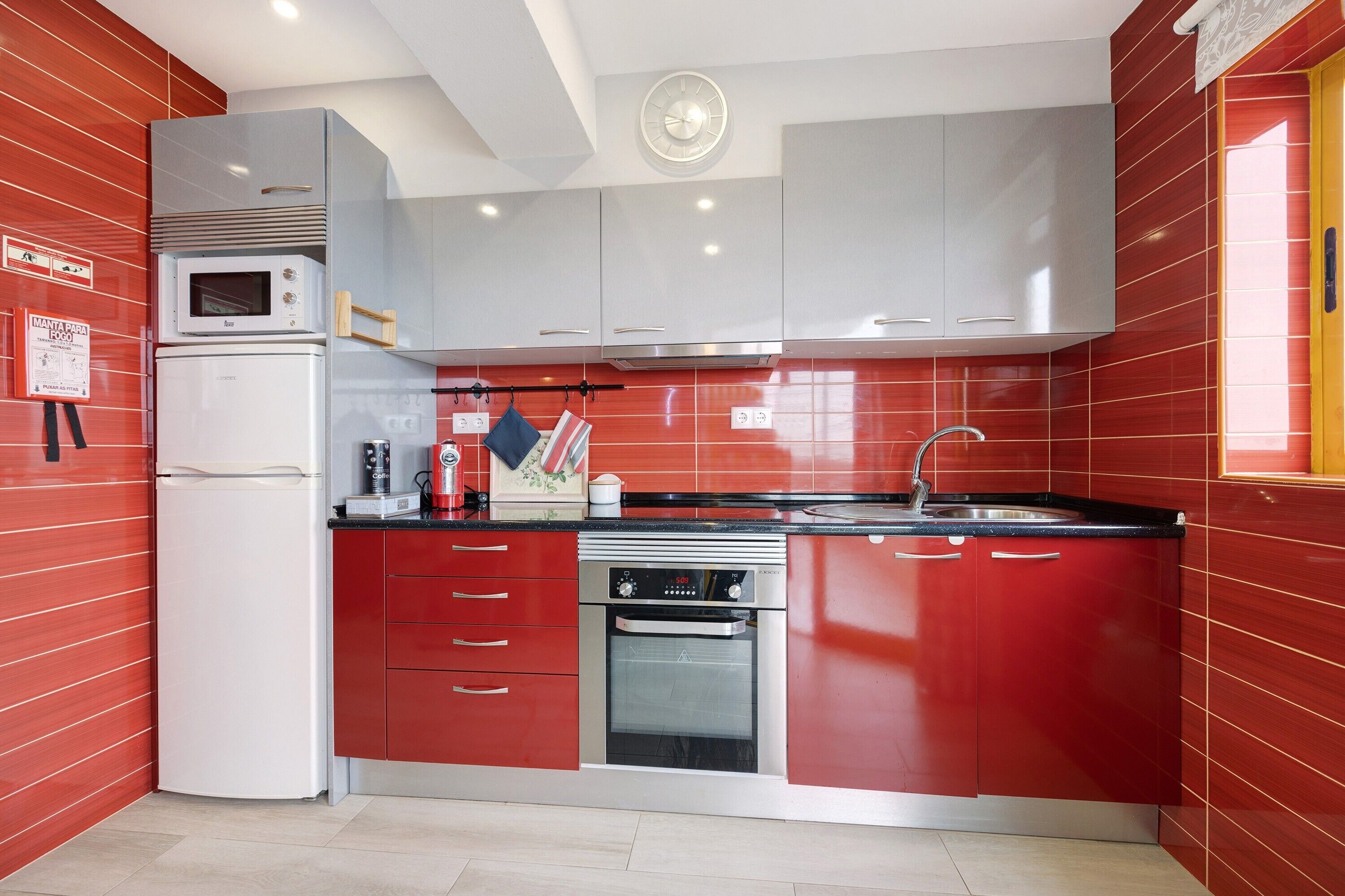 A kitchen with red cabinets, a microwave, a refrigerator, a stove, and a sink.