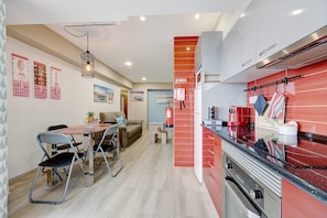Une cuisine moderne avec des meubles de rangement rouges, un coin repas avec une table et des chaises, et un salon avec un canapé.