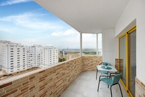 Un balcon avec une table et des chaises, une vue sur les immeubles et une porte vitrée.