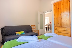 A bedroom with two beds, a wooden wardrobe, a chair, and a door leading to a dining area.