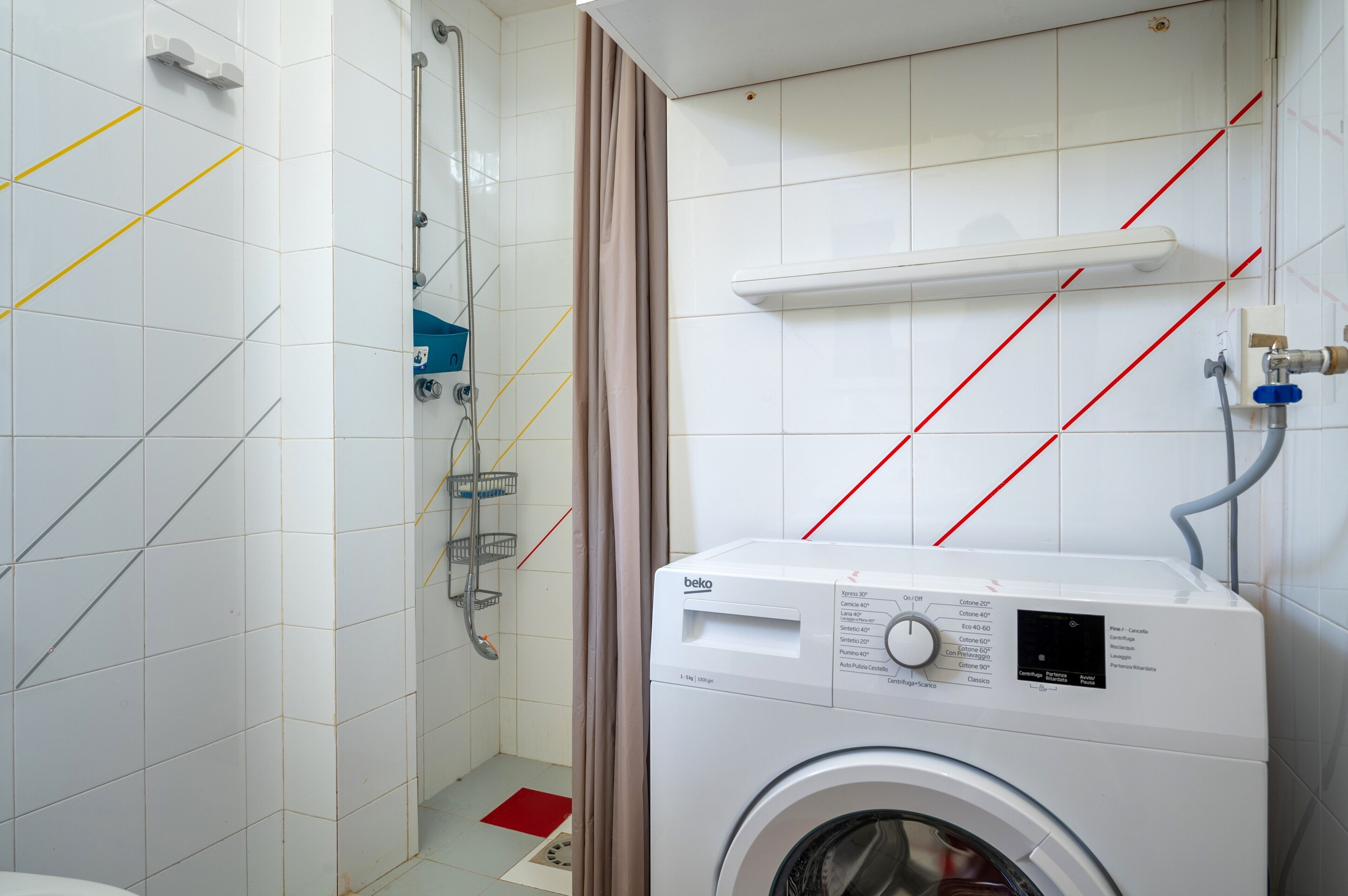 A laundry area with a washing machine, a shower, and a towel rack.