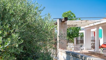 Un'area salotto all'aperto coperta, con una pergola, un muro in pietra e vista su un edificio con una porta rossa.