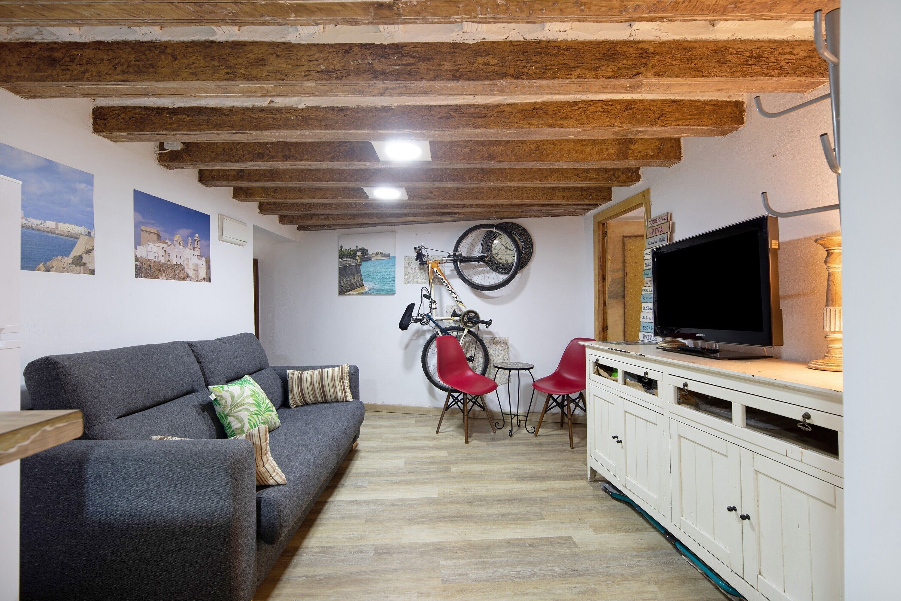 Un salón con sofá, sillas rojas, televisor, bicicleta y vigas de madera en el techo.