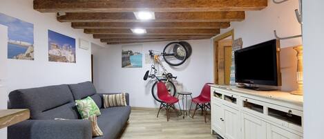 Un salón con sofá, sillas rojas, televisor, bicicleta y vigas de madera en el techo.