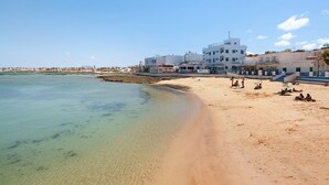A beach with clear water, a sandy shore, and buildings in the background. - Vacation Apartment 'Central Bright Studio' (Corralejo)