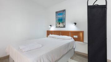 Un dormitorio con una cama, un cuadro de una playa, un cabecero de madera y un objeto negro en la pared.