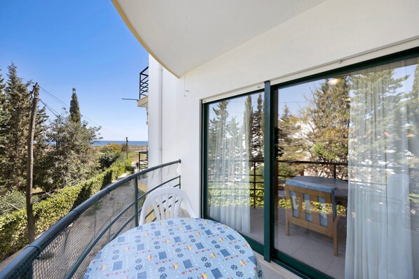 A balcony with a table and chair, a view of trees and a building, and a clear sky.