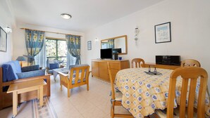 A room with a sofa, a dining table with chairs, a TV, and a cabinet.