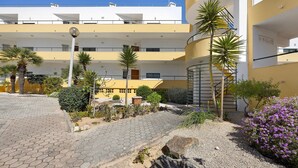 A multi-story building with balconies, a spiral staircase, and a paved courtyard with palm trees and shrubs.