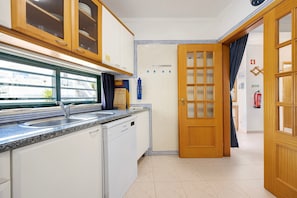 Une cuisine équipée d’un lave-vaisselle, d’une fenêtre et d’une porte donnant sur une autre pièce.