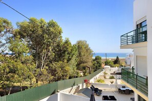 A balcony with outdoor furniture, a view of the sea, and a green fence.