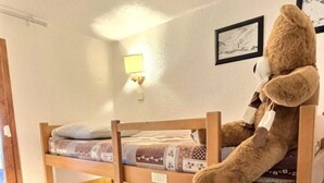 Et soveværelse med køjeseng, hvor der ligger en bamse i overkøjen, og et lille bord med en lampe.