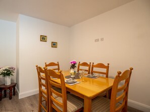 Une salle à manger avec une table et des chaises en bois, un vase rempli de fleurs et deux tableaux encadrés accrochés au mur.
